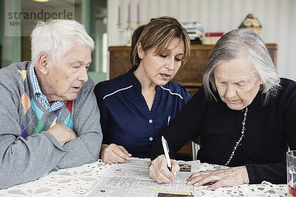 Hausmeisterin unterstützt Seniorin bei der Lösung von Kreuzworträtseln im Pflegeheim