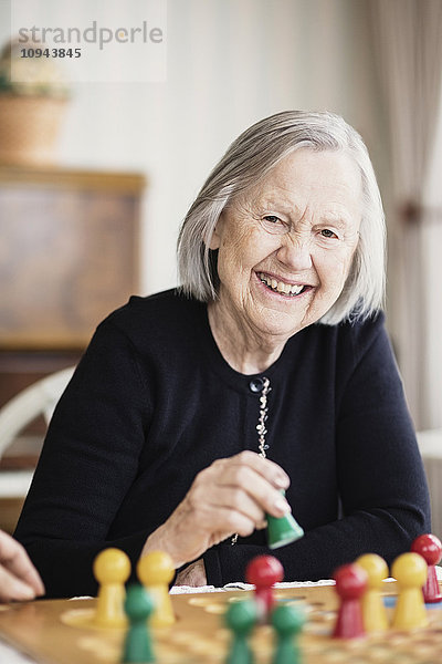 Porträt einer glücklichen Seniorin  die Ludo im Pflegeheim spielt
