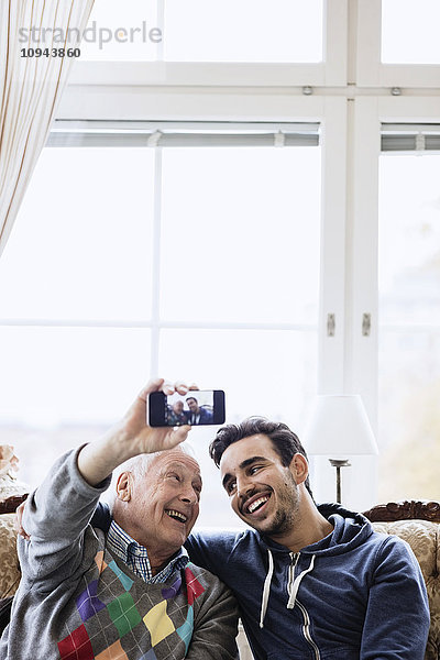 Glücklicher Mann nimmt Selfie mit jungem Betreuer im Pflegeheim