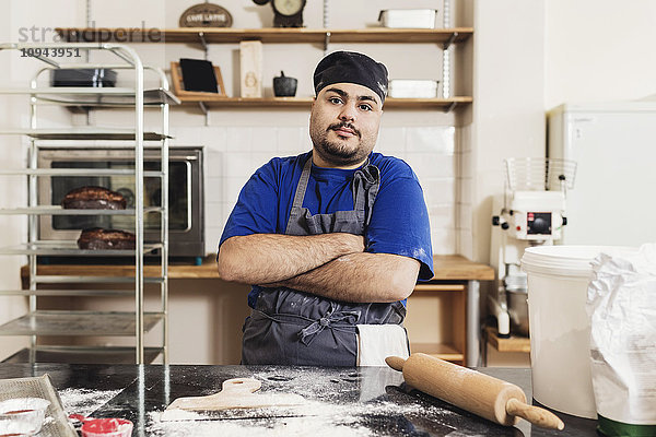 Porträt eines jungen Mannes  der mit gekreuzten Armen in der Küche steht.