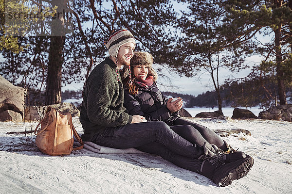 Ein glückliches Paar genießt den Kaffee beim Entspannen auf dem schneebedeckten Feld.
