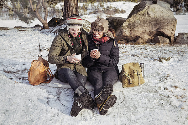 Glückliches Paar beim Kaffeetrinken auf dem schneebedeckten Feld