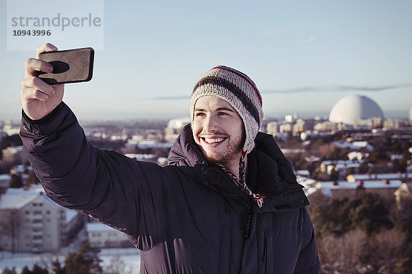 Lächelnder junger Mann klickt Selfie durch Smartphone im Winter