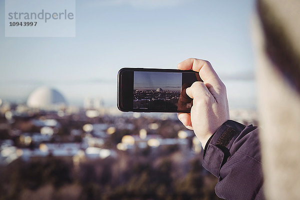 Beschnittenes Bild eines Mannes  der im Winter das Stadtbild mit dem Handy fotografiert.