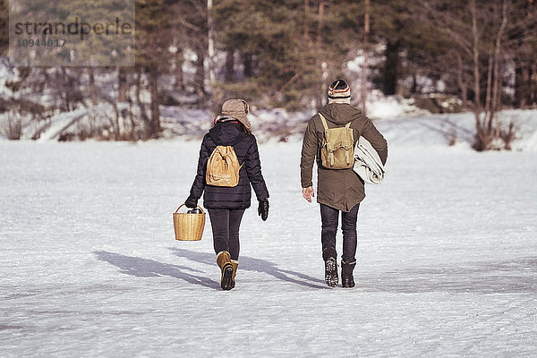 Durchgehende Rückansicht des Paares mit Rucksack auf schneebedecktem Feld