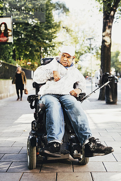 Vorderansicht eines behinderten Menschen im Rollstuhl auf dem Bürgersteig in der Stadt