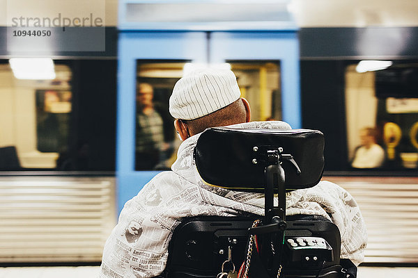 Rückansicht des behinderten Mannes im Rollstuhl gegen den Zug am Bahnhof
