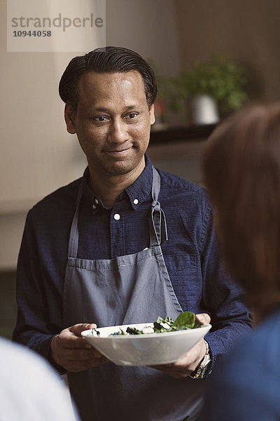 Lächelnder reifer Mann hält Salatschüssel  während er eine Freundin ansieht.