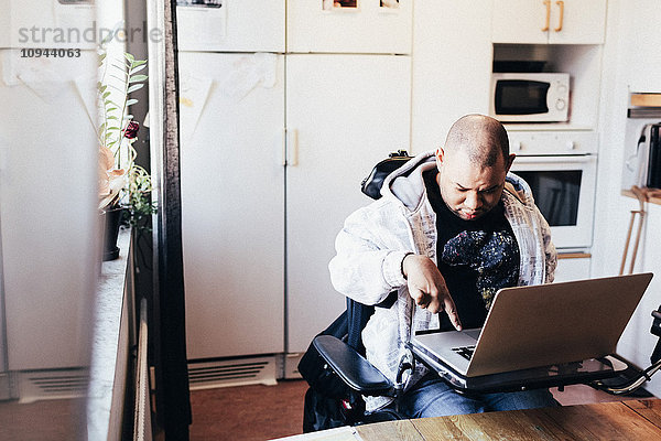 Behinderter Mann mit Laptop im Rollstuhl im Aufnahmestudio