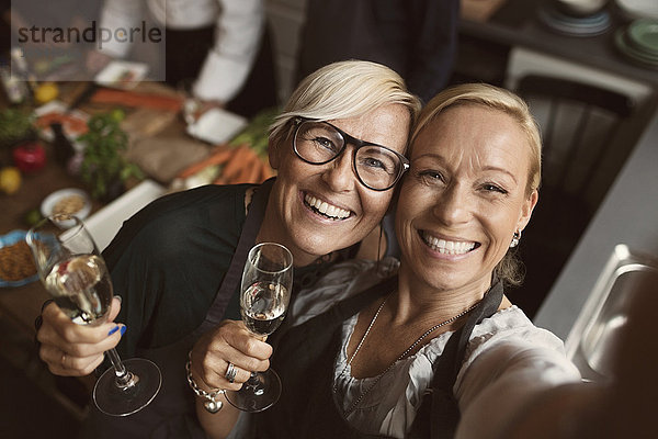 Fröhliche reife Frauen  die Champagnerflöten halten  während sie Selfie in der Küche nehmen.