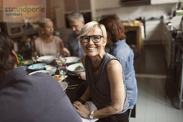 Porträt einer fröhlichen reifen Frau  die mit Freunden am Tisch sitzt.