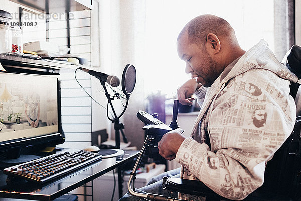 Behinderter Musiker beim Betrachten des Joysticks am Rollstuhl im Aufnahmestudio