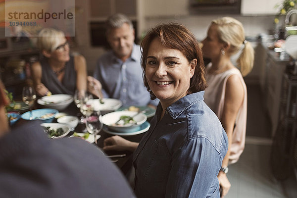 Portrait einer fröhlichen reifen Frau  die mit Freunden am Tisch sitzt.