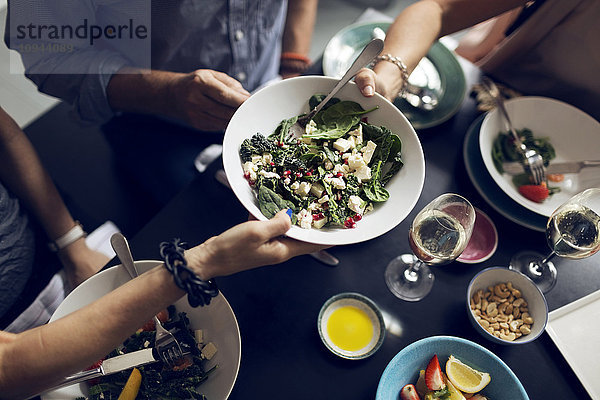 Abgeschnittenes Bild von Freunden  die eine Salatschüssel am Tisch halten.