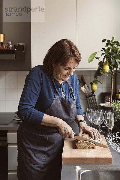 Lächelnde Frau beim Brotschneiden in der Küche