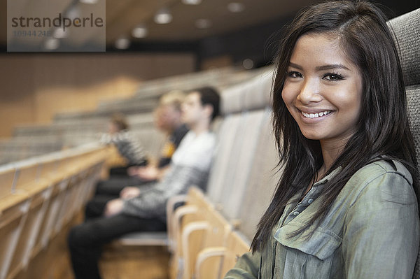 Porträt einer glücklichen jungen Frau im Auditorium mit Freunden im Hintergrund