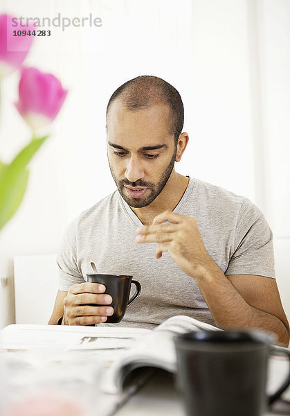 Vorderansicht eines erwachsenen Mannes  der Zeitung liest  während er eine Tasse Kaffee hält.