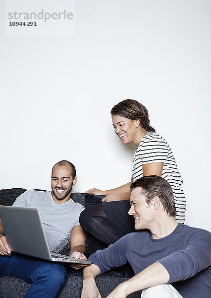 Drei mittelgroße erwachsene Freunde  die zusammen einen Laptop benutzen.