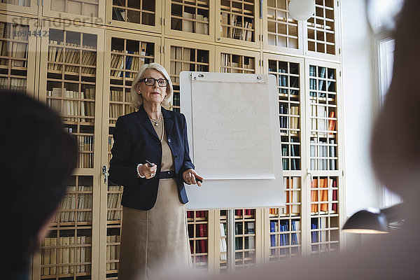 Seniorin beim Präsentieren im Stehen am Bücherregal