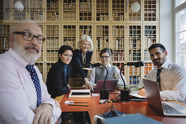 Porträt glücklicher Anwälte am Tisch gegen das Bücherregal