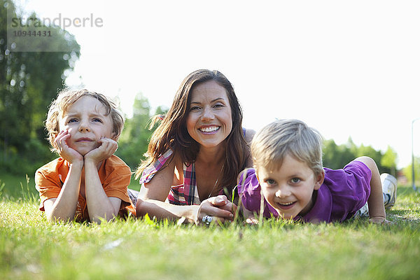 Porträt einer glücklichen Mutter und Kinder auf Gras liegend