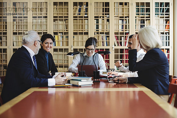 Glückliche Anwältinnen und Anwälte sitzen im Vorstandszimmer gegen das Bücherregal.