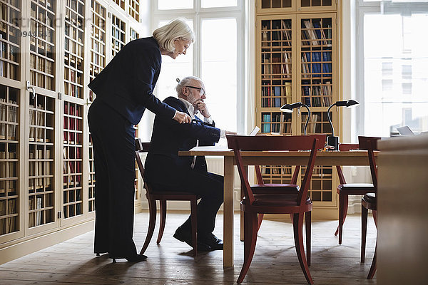 Seitenansicht einer älteren Anwältin und eines älteren Anwalts bei Tisch in der Bibliothek