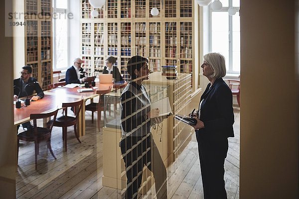 Juristinnen diskutieren im Stehen durchs Glas in der Bibliothek