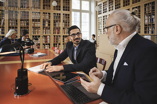 Lächelnder Mann im Gespräch mit dem leitenden Anwalt bei Tisch in der Bibliothek