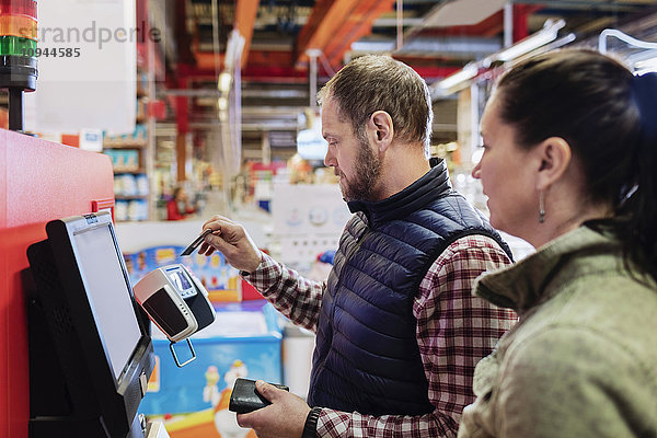 Mann  der mit Kreditkarte bezahlt  während er mit einer Frau im Supermarkt steht.