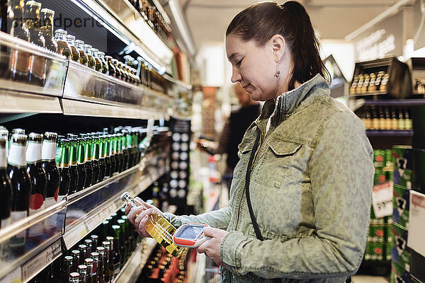 Seitenansicht der Frau beim Scannen von Bierflaschen im Supermarkt