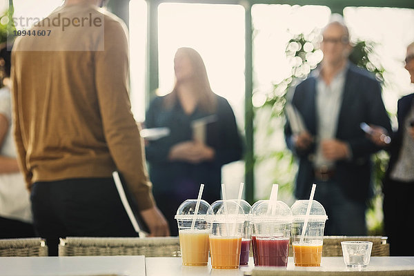 Fruchtsaft in Plastikbechern auf dem Tisch mit Geschäftsleuten im Hintergrund im Büro