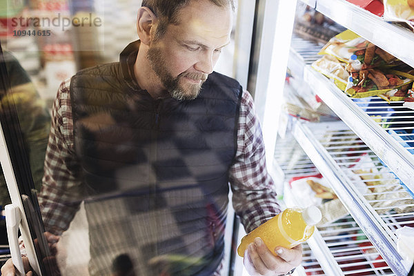 Hochwinkelansicht des männlichen Kunden beim Lesen des Getränkeetiketts im Kühlbereich