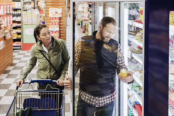 Paare kaufen Lebensmittel  während sie im Supermarkt am Kühlschrank stehen.