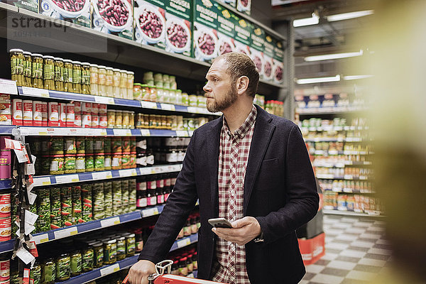 Männlicher Kunde mit Smartphone beim Einkaufen im Lebensmittelgeschäft