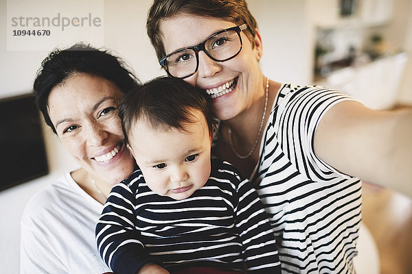 Porträt eines lächelnden lesbischen Paares mit Kleinkind zu Hause