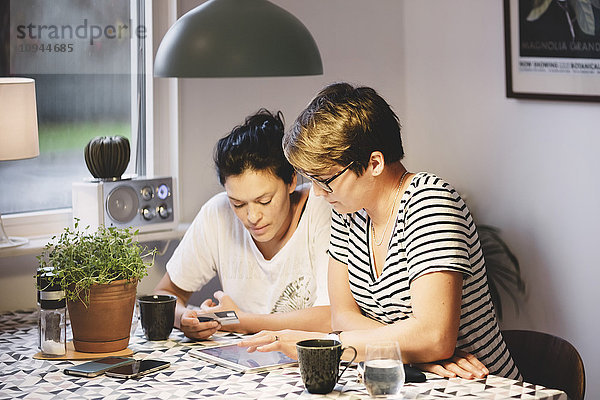 Lesbenpaar beim Sitzen am Esstisch mit digitalem Tablett