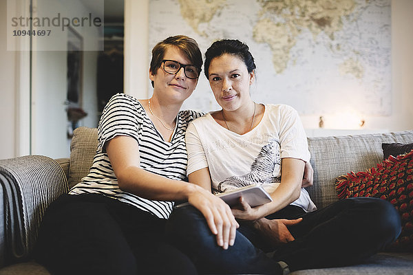 Porträt eines lächelnden lesbischen Paares  das zu Hause im Wohnzimmer sitzt.
