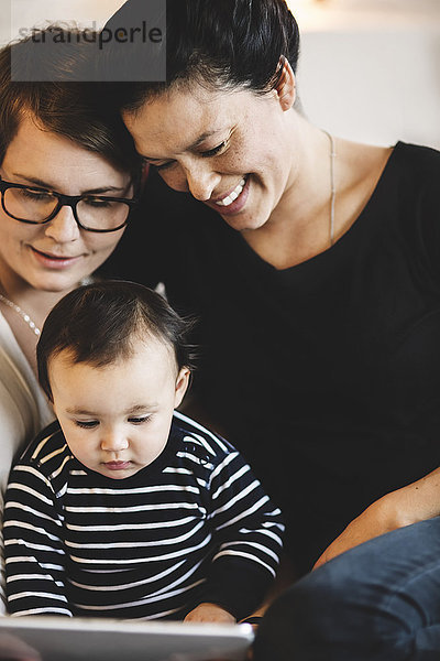 Lächelnde Frauen mit Kleinkind im digitalen Tablett  während sie zu Hause sitzen.