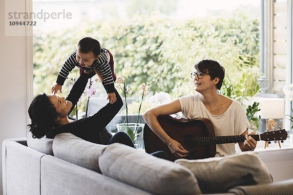 Mutter genießt mit dem kleinen Mädchen  während die Frau zu Hause Gitarre spielt.