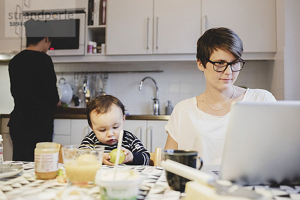 Mutter mit Laptop neben Baby Girl während der Arbeit in der Küche