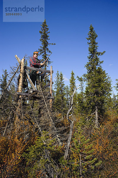 Jäger stehend mit Gewehr auf Holzturm im Wald