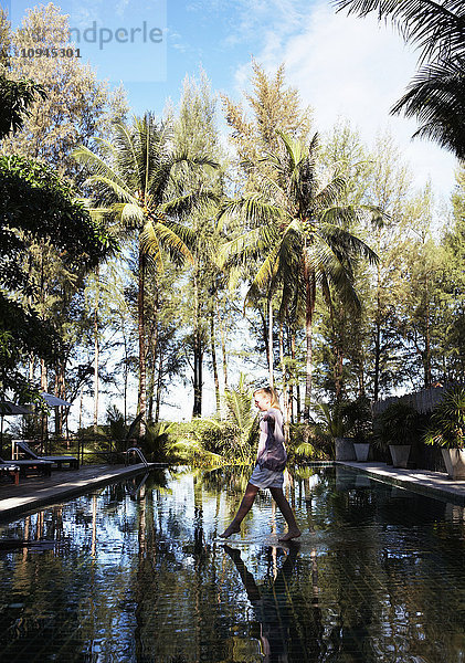 Thailand  Frau überquert Wasserbecken mit spiegelnden Palmen