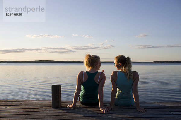Zwei Frauen sitzen in der Abenddämmerung auf einem Pier  Rückansicht