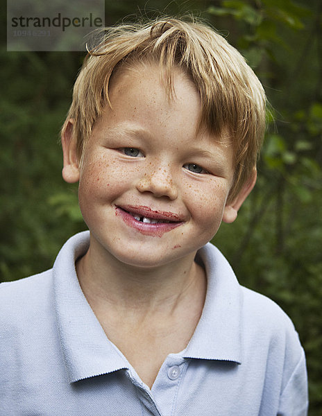 Junge mit Blaubeersaft im Gesicht  Nahaufnahme  Porträt  lächelnd
