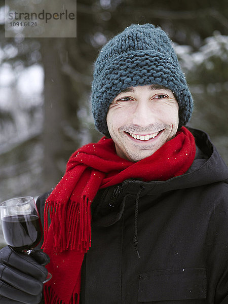 Porträt eines Mannes in Winterkleidung  der ein Glas Rotwein hält
