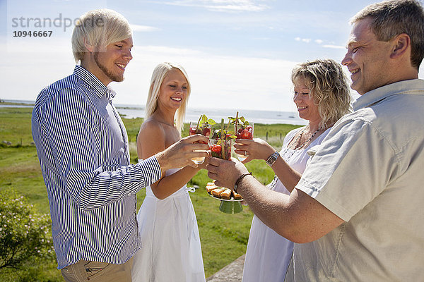 Paare stoßen lächelnd auf ein Getränk an der Küste an