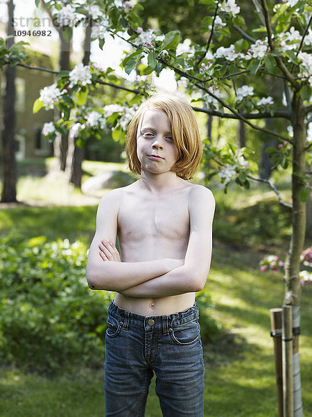 Junge steht ohne Hemd neben einem Baum