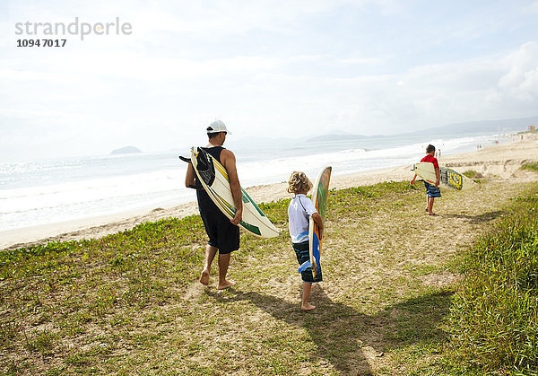 Zwei Jungen und ein Mann gehen am Strand mit Surfbrettern spazieren