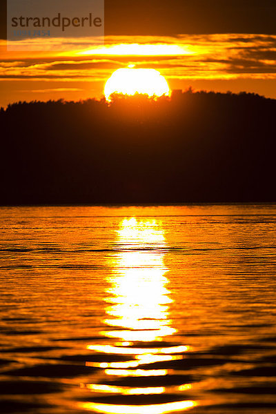 Orangefarbene Sonne  die sich bei Sonnenuntergang im Wasser spiegelt